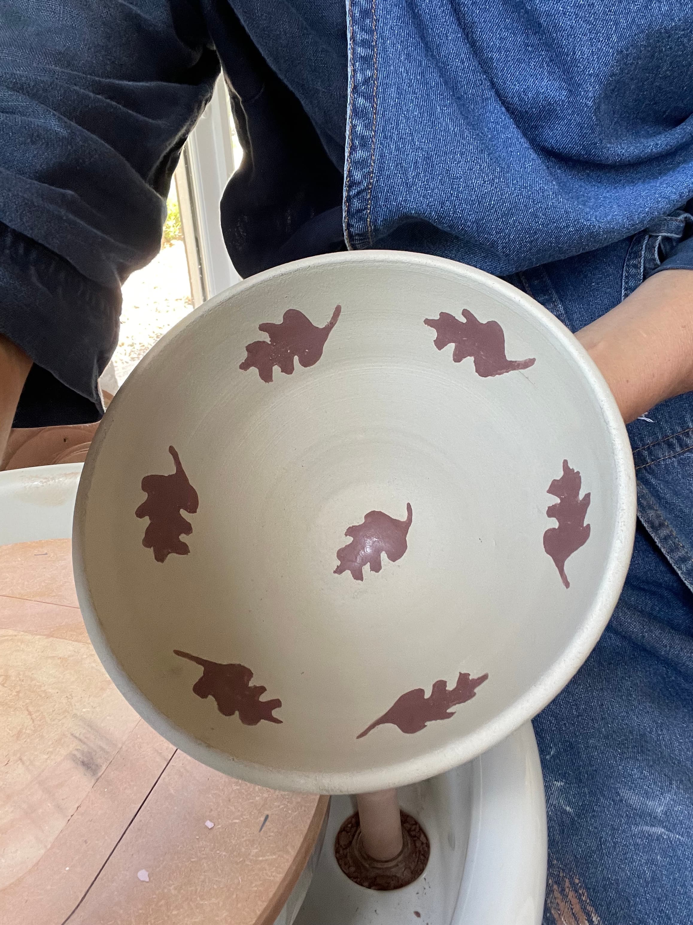 A slip-coated bowl stamped with oak leaves, held up fresh from decorating
