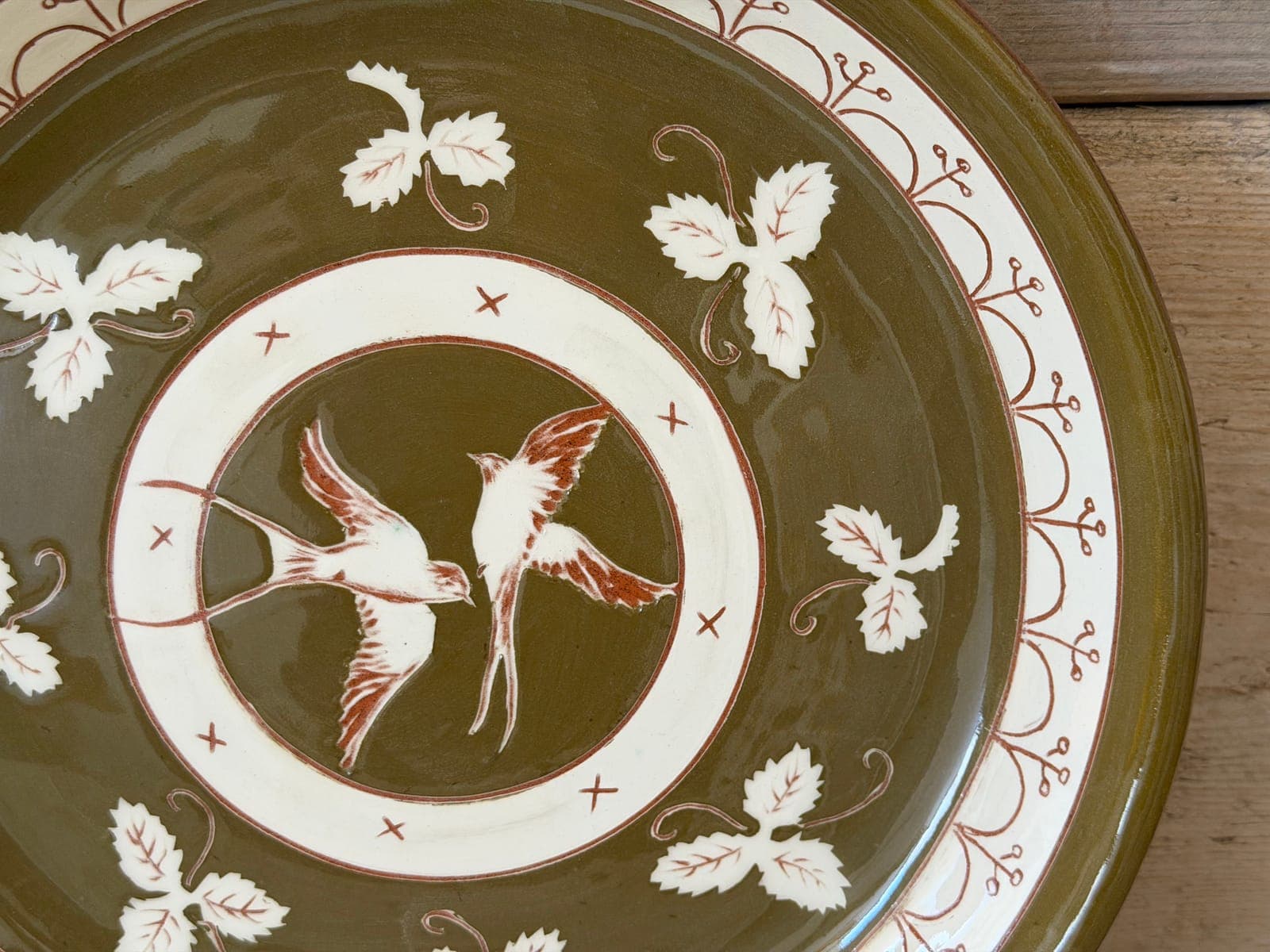 Two sgraffito swallows at the centre of an olive-green slipware plate