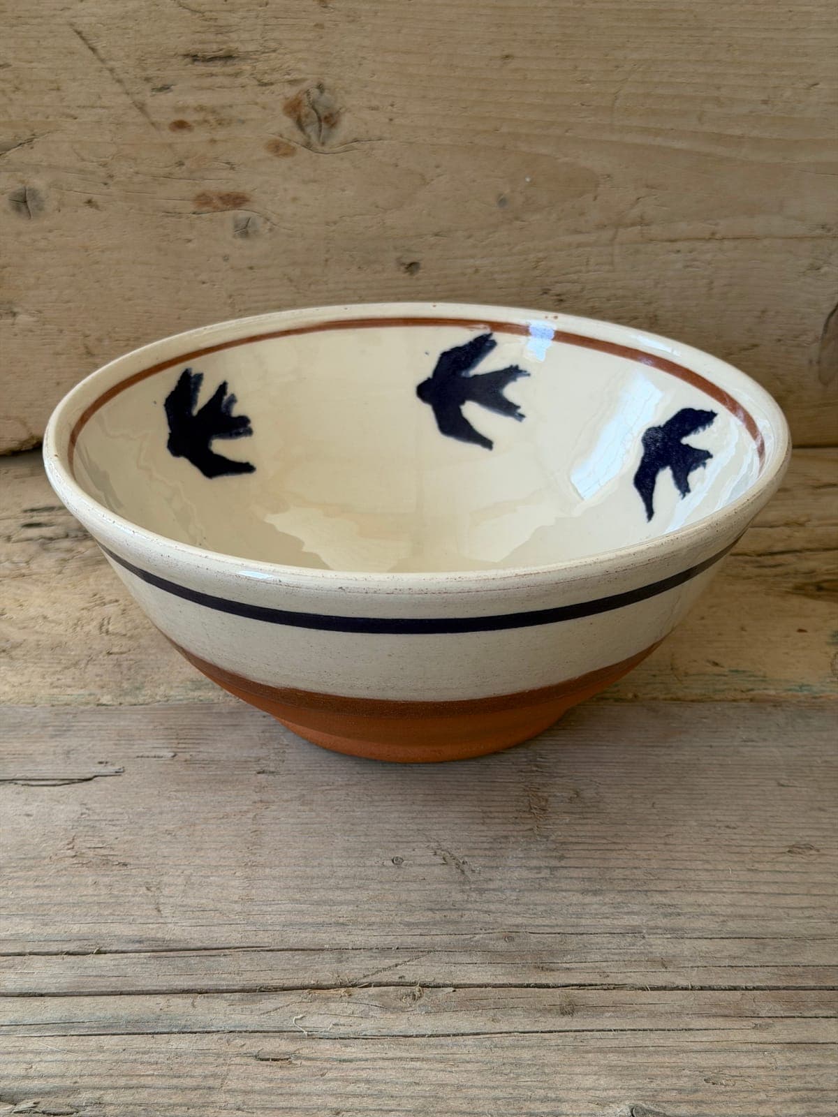 Swallows slipware bowl in cream with dark blue swallows inside, terracotta band and foot